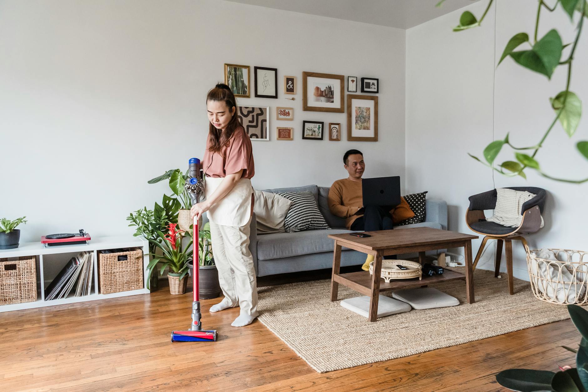 a man working from home and a woman vacuuming in a living room