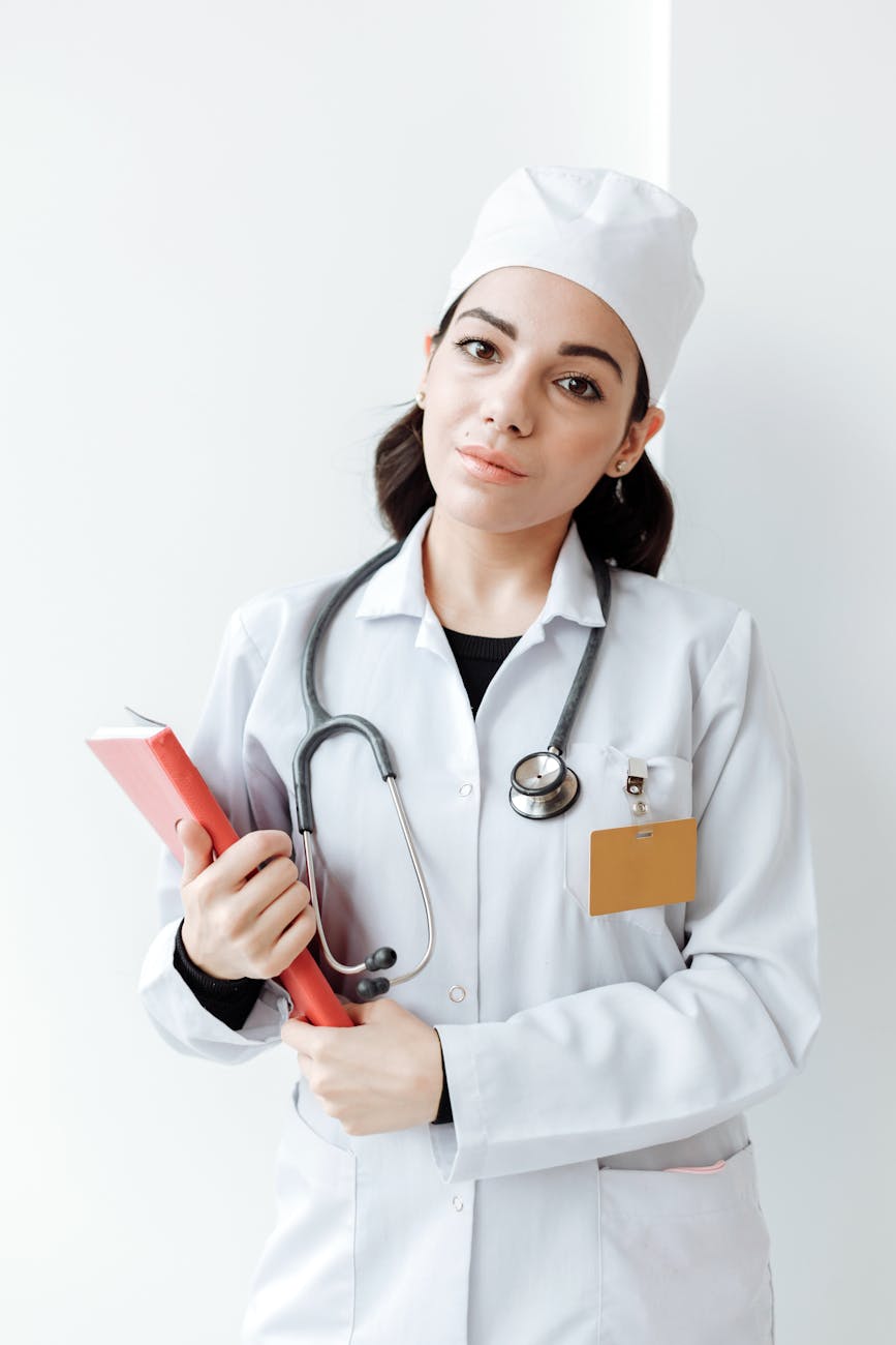 healthcare professional in white uniform with stethoscope hanging on her neck holding a book while looking at the camera